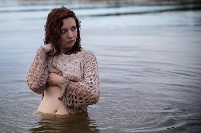 Lia in a knit sweater standing in shallow water