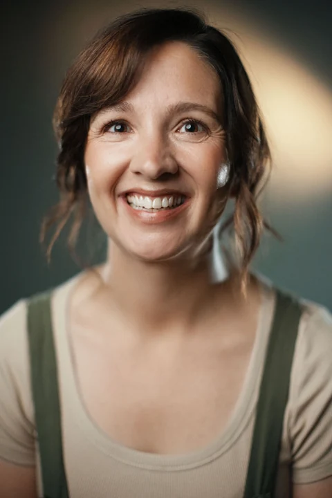 Lia smiling in an olive pinafore and cream top