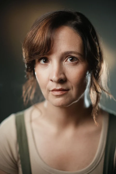Lia in an olive pinafore and cream top, looking directly at the camera