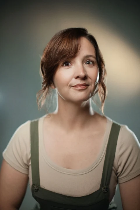 Lia in an olive pinafore and cream top, looking to the side