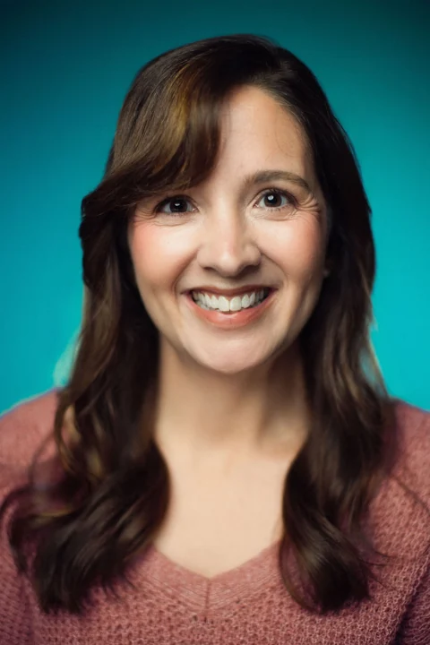 Lia smiling in a rose sweater against a teal background
