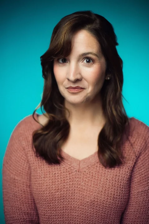 Lia in a rose sweater against a teal background