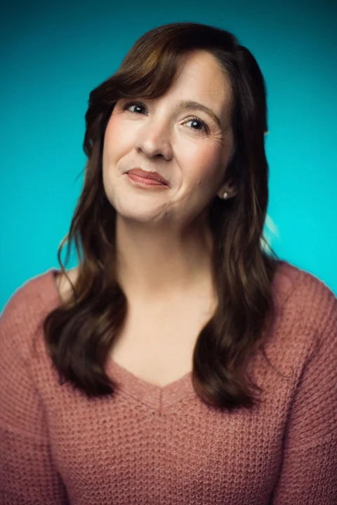 Lia in a rose sweater with her head tilted against a teal background