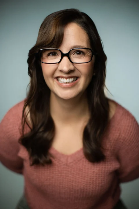 Lia smiling in glasses and a rose sweater