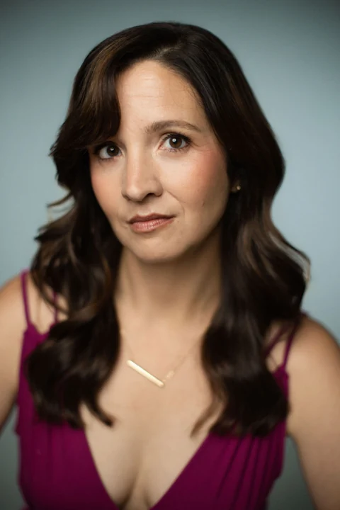 Lia in a plum top and gold necklace, looking into the camera